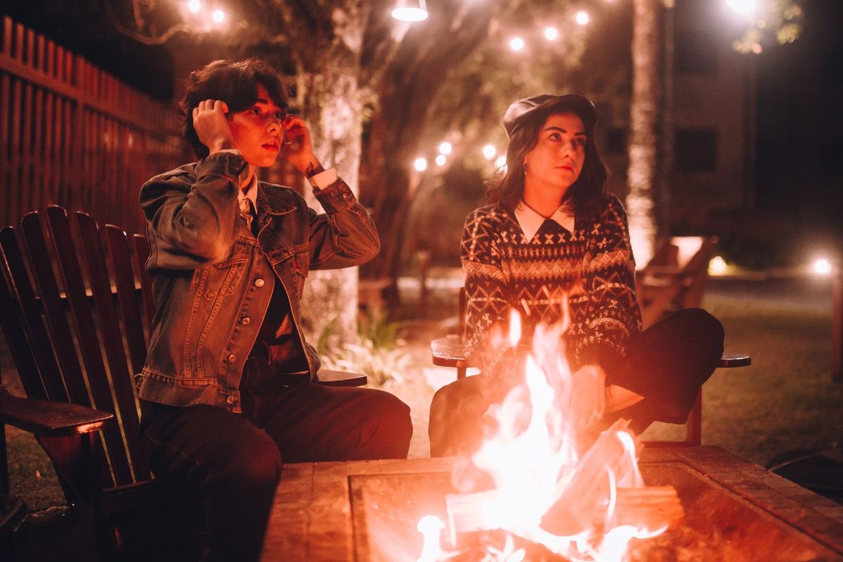 Two people sitting beside a fire pit at night under string lights