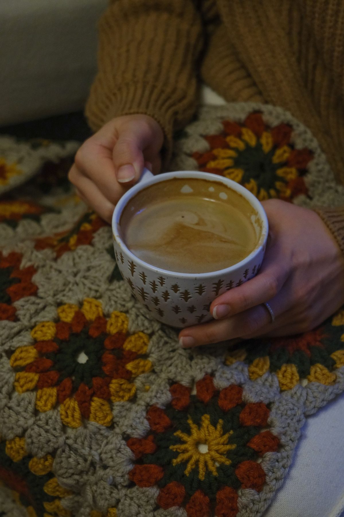 Hands holding a mug of coffee over a colorful crocheted blanket