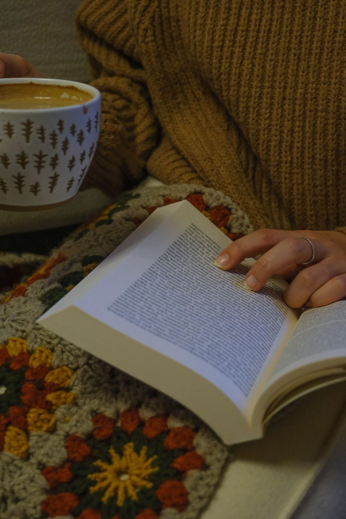 An open book and a mug of coffee resting on a knitted blanket