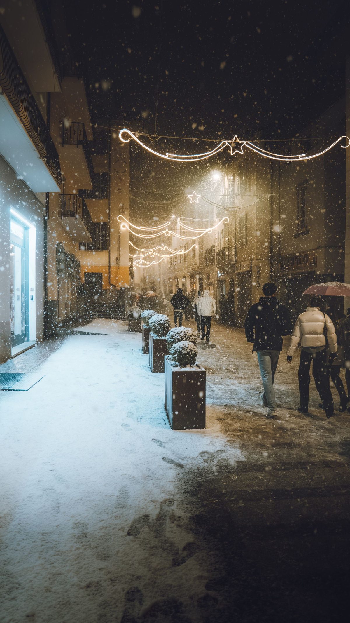 A snow-covered street strung with Christmas lights in the evening