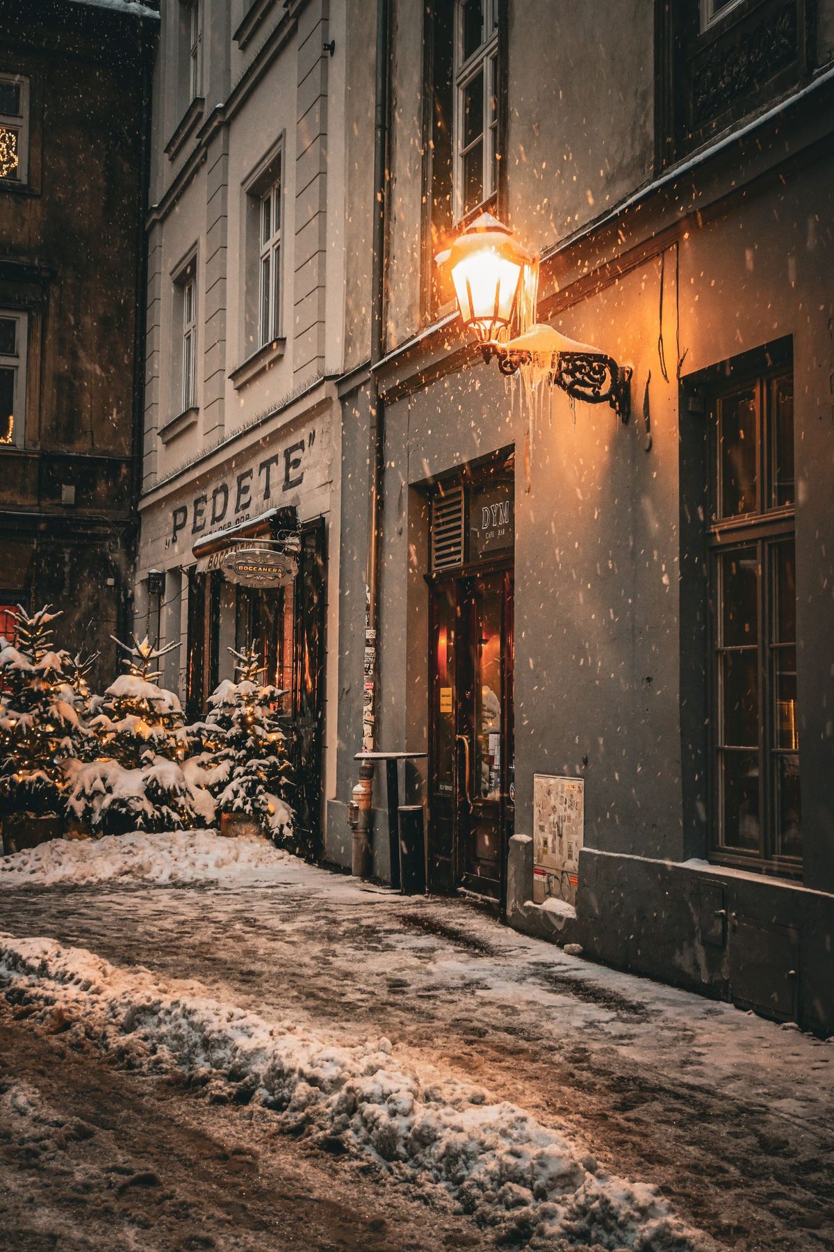 A lit street lamp on a snow-covered old town street at night