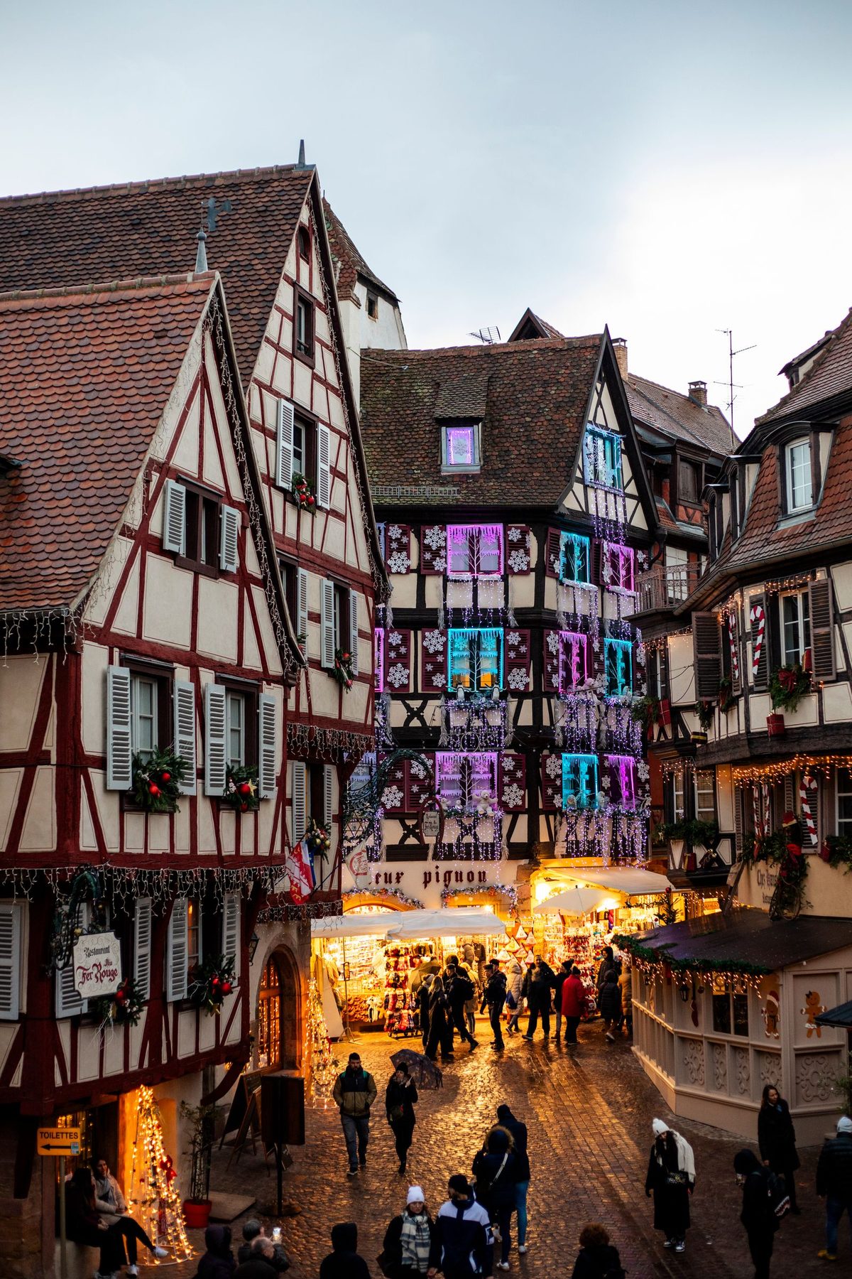 Half-timbered houses and Christmas market stalls in Colmar, France, lit at dusk