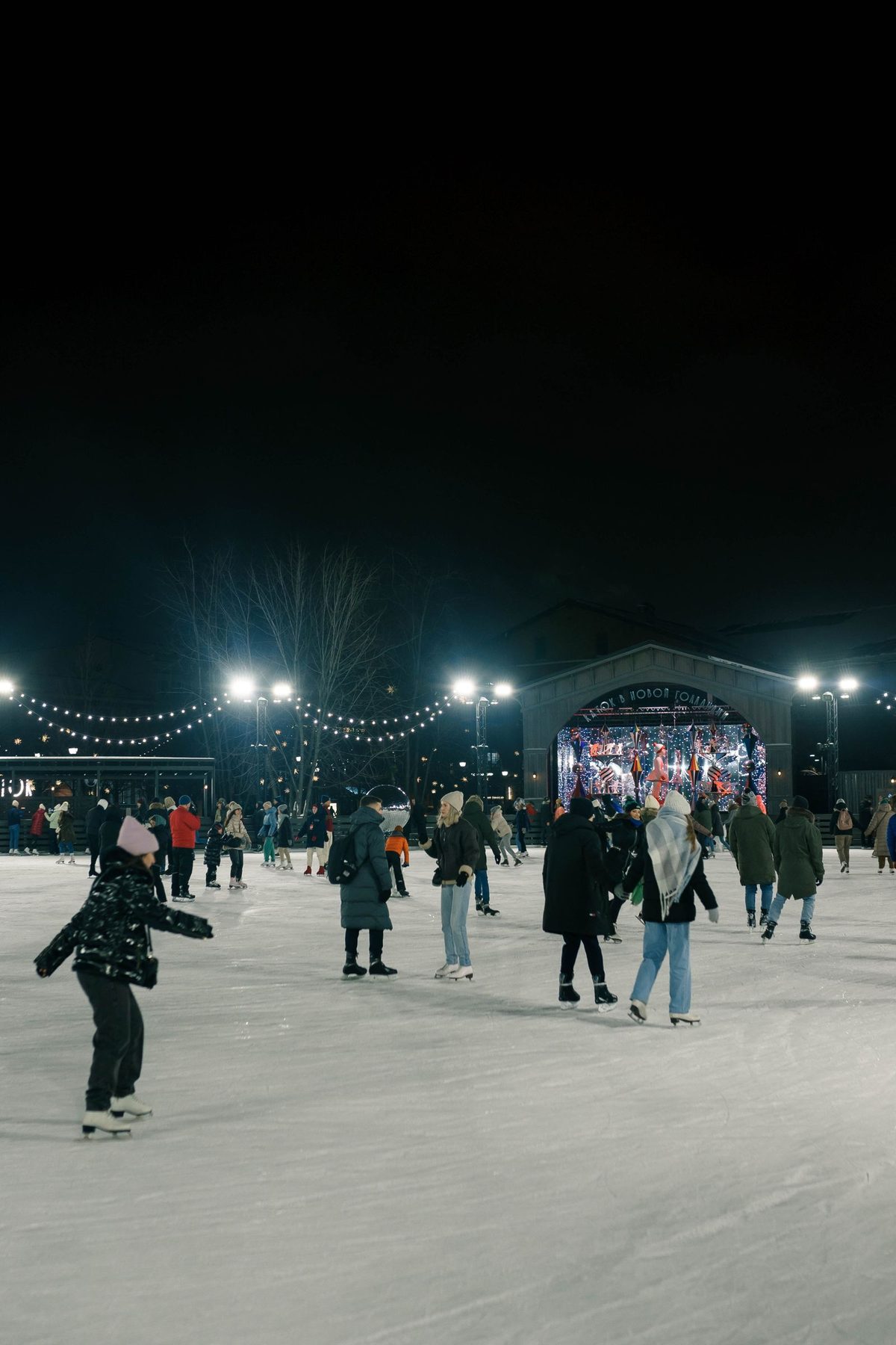 People skating on an outdoor ice rink lit up at night